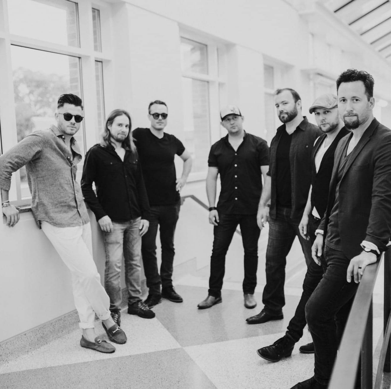 Seven men pose in a sunlit hallway, dressed for Gameday Sports Bar Restaurant Appleton fun.