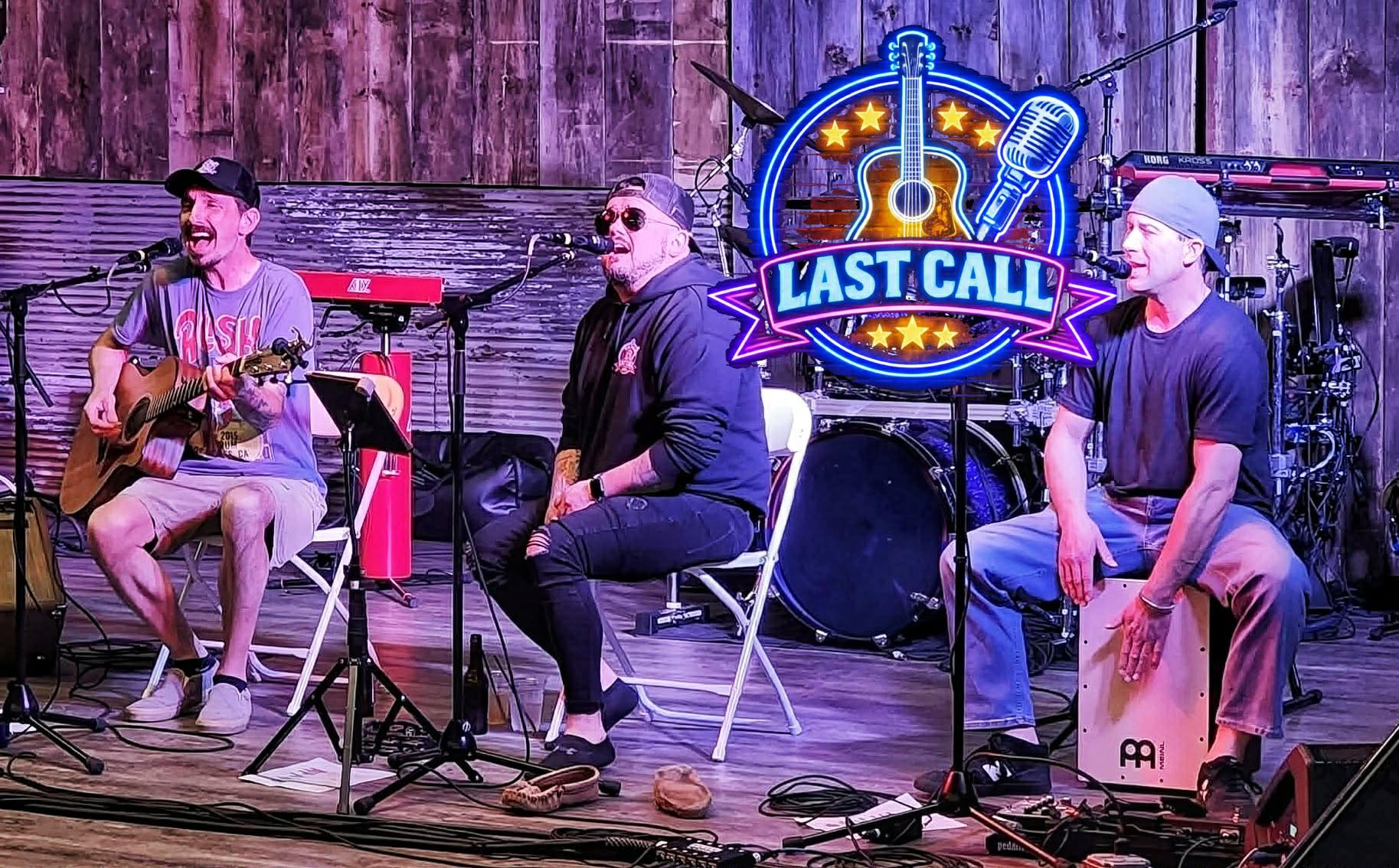Three men on stage, one singing and playing guitar, one singing, one playing percussion.