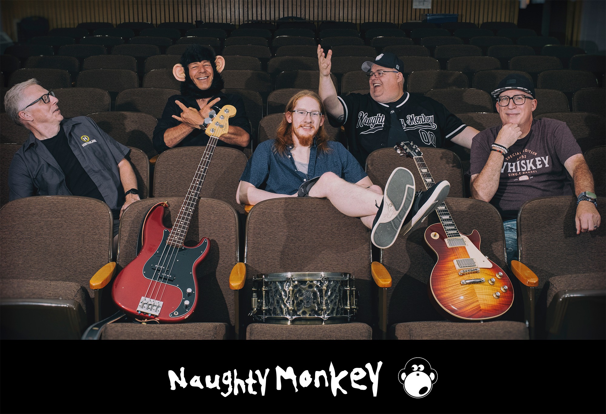 The band Naughty Monkey poses in theater seats with guitars and a drum.